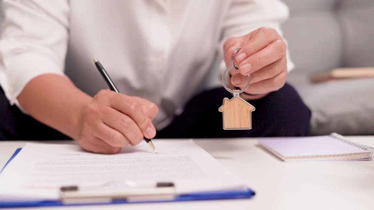 A homeowner signs mortgage documents and holds a house-shaped keychain.