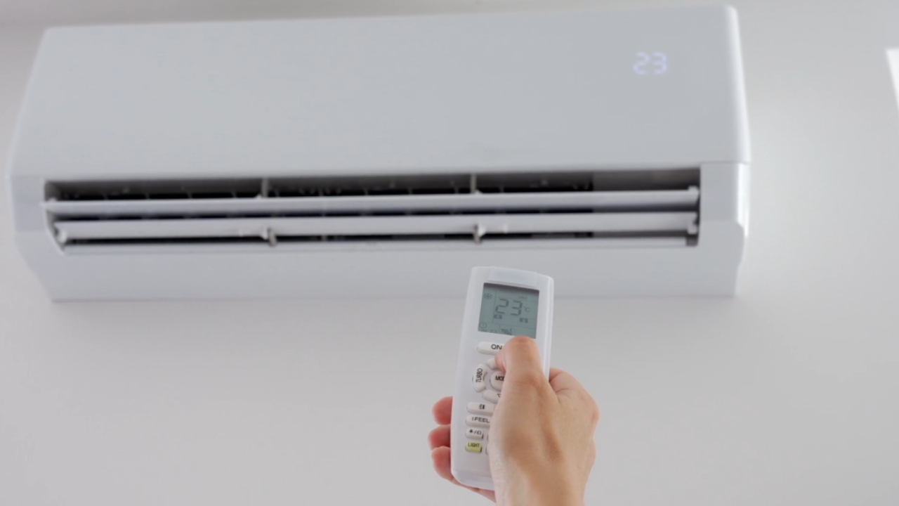 A person sets a wall-mounted air conditioner to 23°C with a remote.