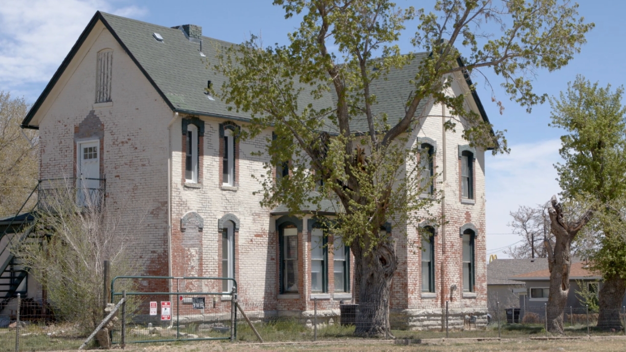 Older brick house with a weathered exterior and mature trees.