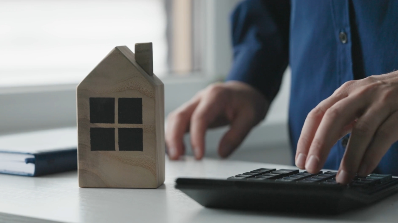 A homeowner uses a calculator beside a small wooden house model.