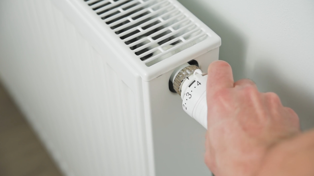 A person adjusts the thermostat valve on a white radiator.