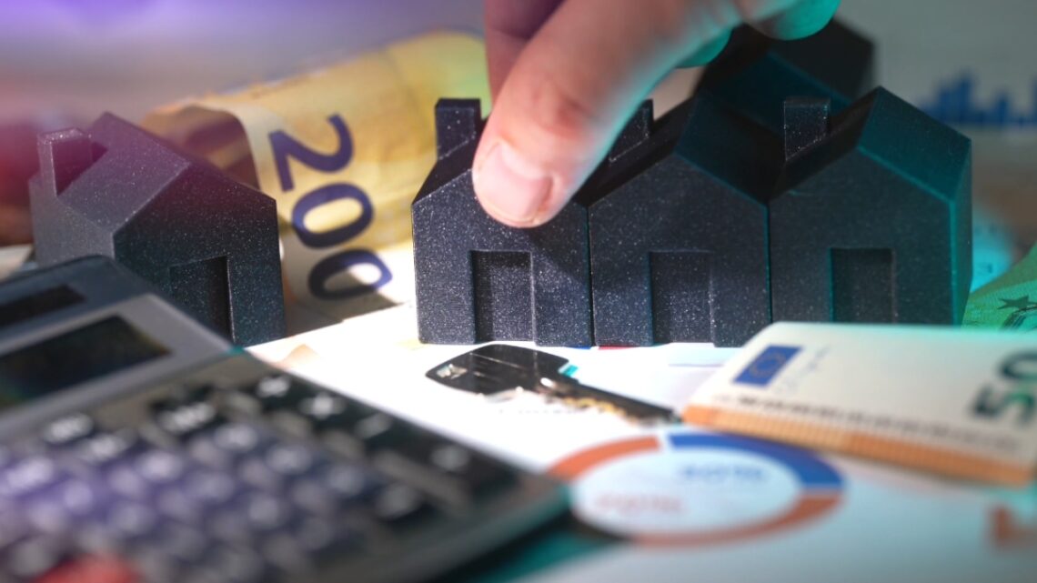 Small house models sit beside cash, a calculator, and home finance documents.