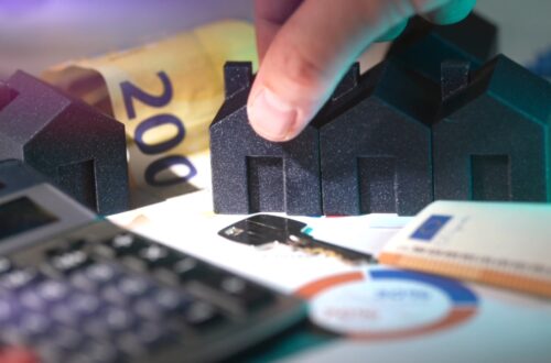 Small house models sit beside cash, a calculator, and home finance documents.