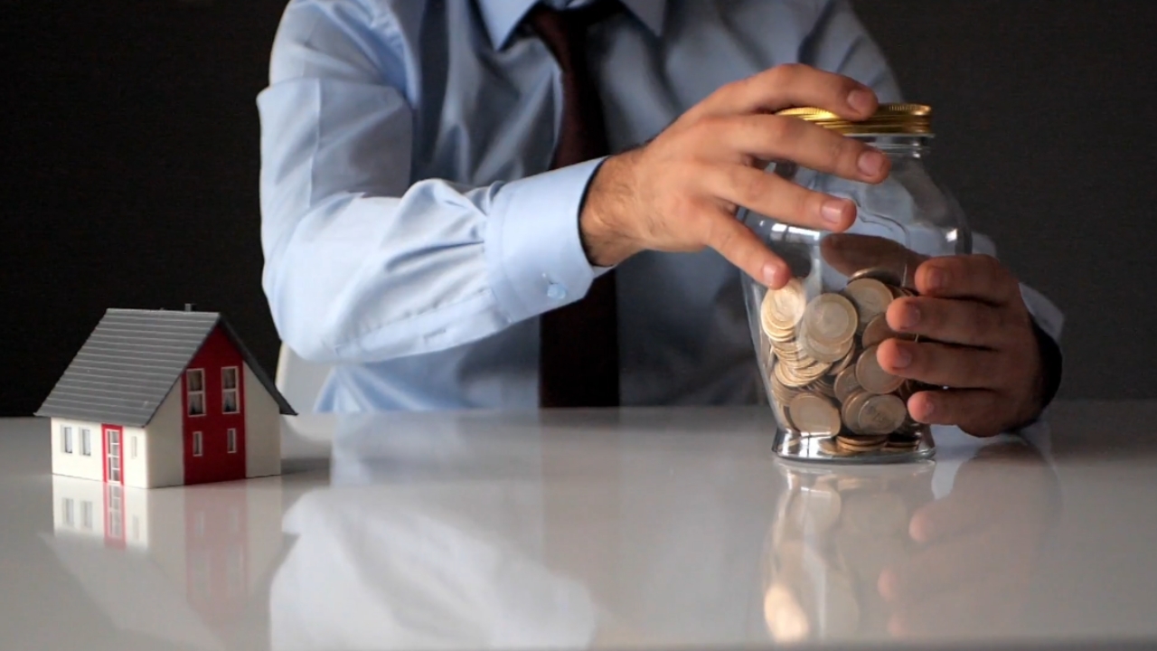 Man adds coins to a savings jar beside a model house.