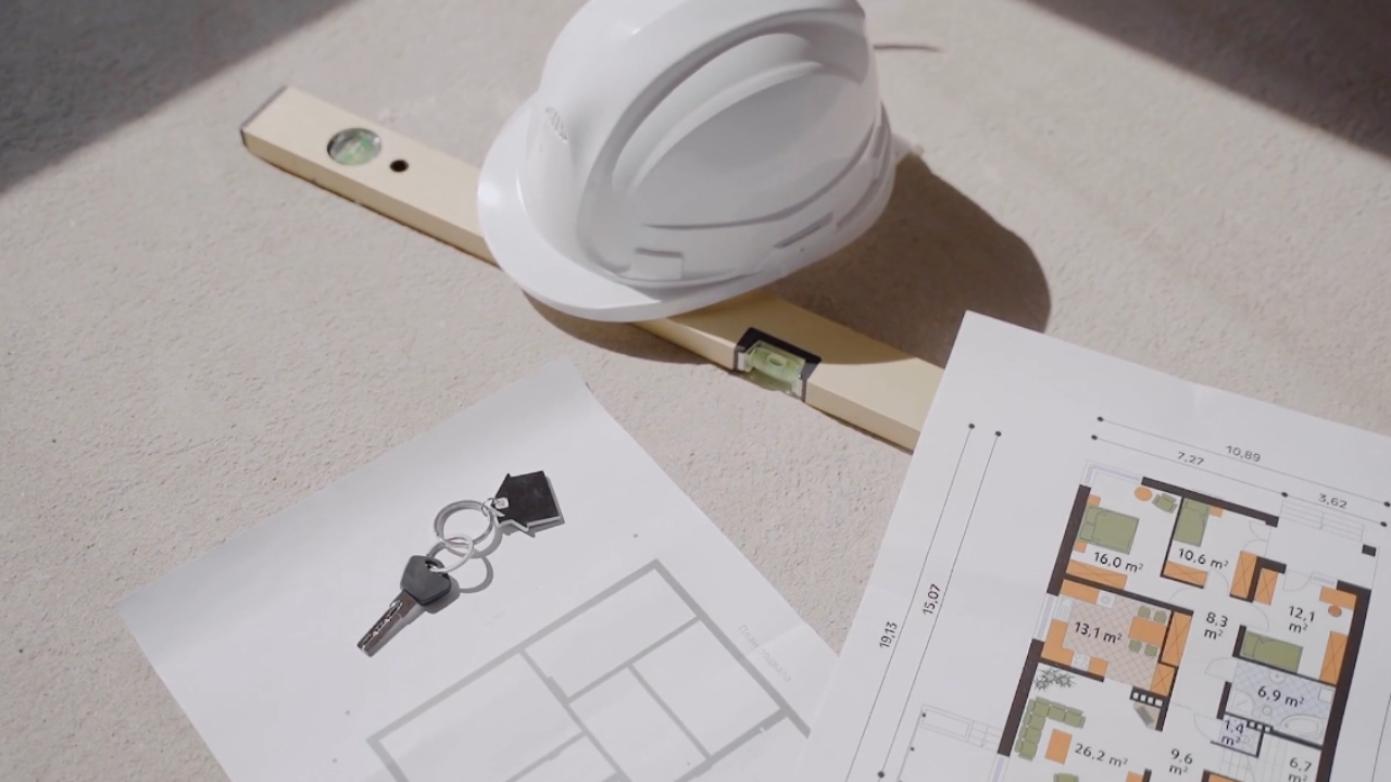 Renovation plans, a hard hat, level, and house keys lie on a work surface.