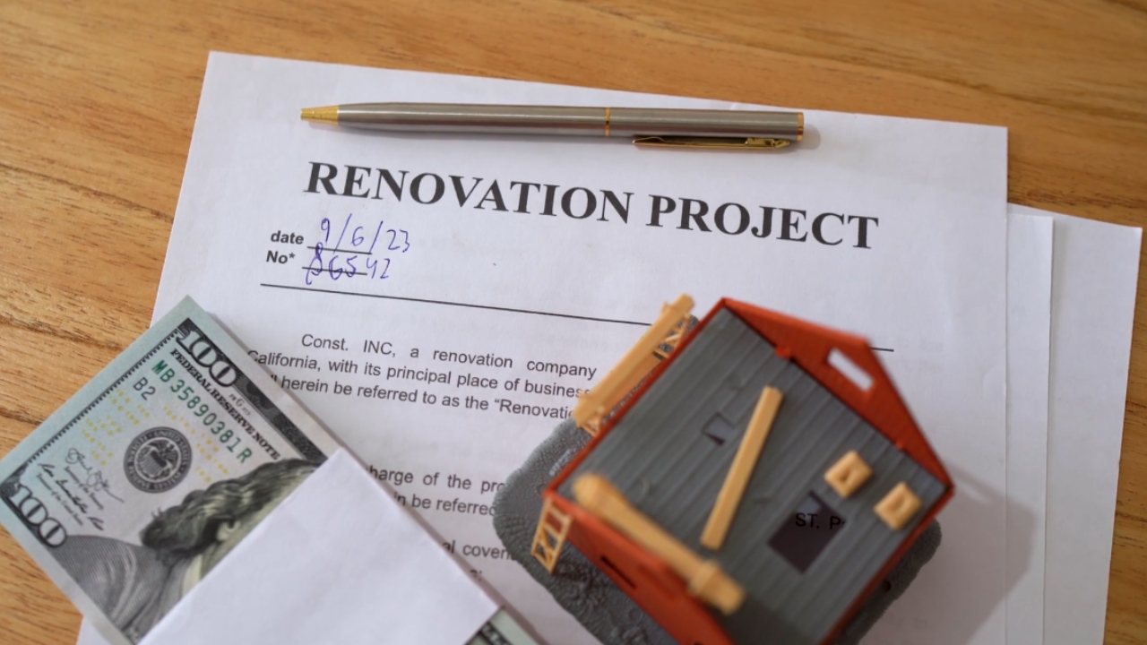 Renovation contract, cash, and a model house sit on a table.