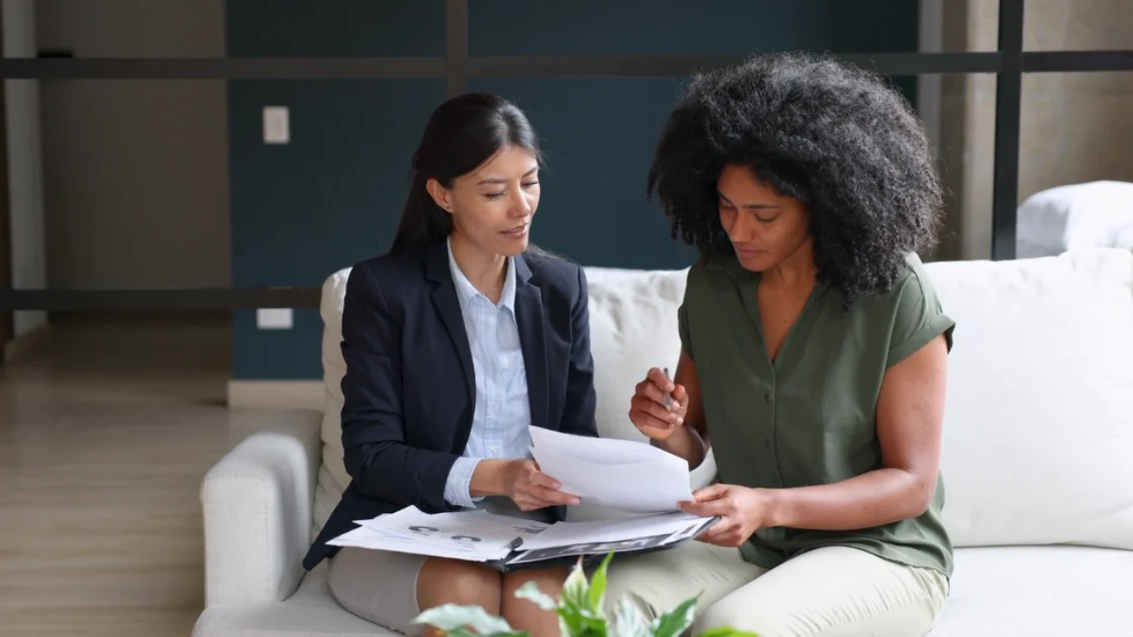 An insurance agent reviews home insurance documents with a homeowner on a sofa.