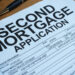 A second mortgage application form sits on a wooden desk beside a pen and glasses.