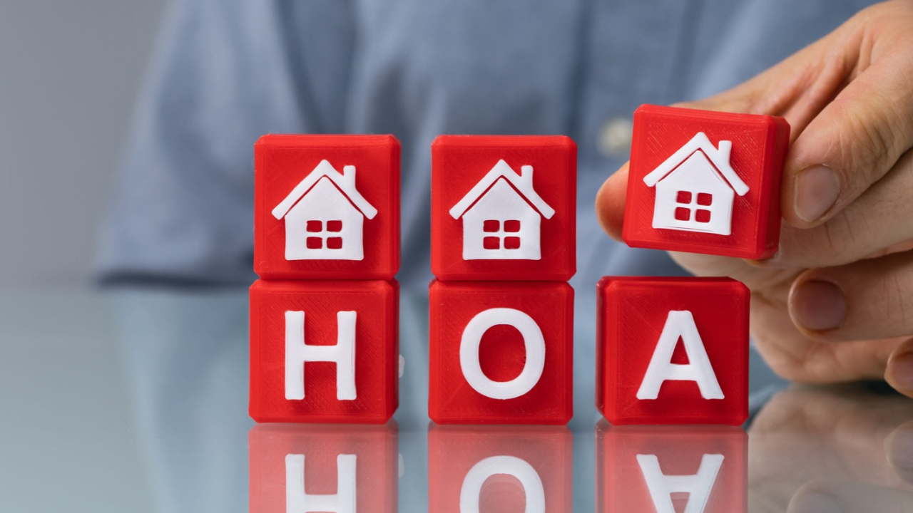 A hand places a red house block above HOA letter blocks on a table.