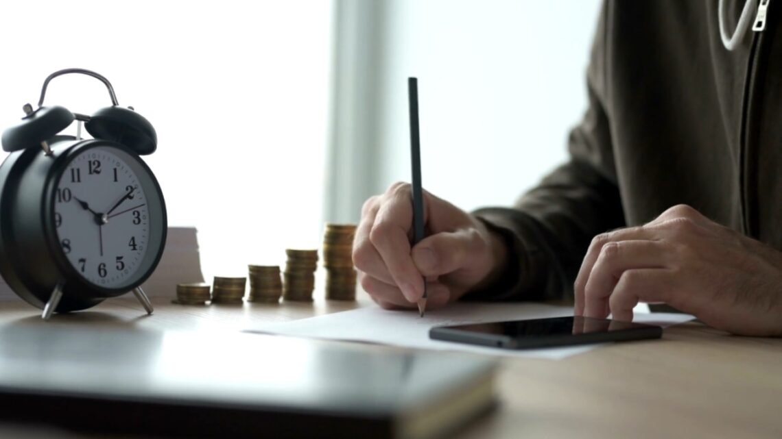 A homeowner calculates renovation costs beside a clock and stacks of coins.