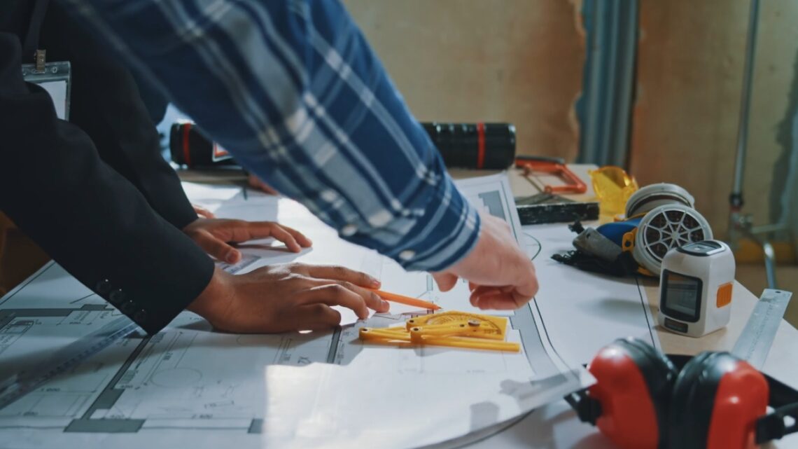 Two people review renovation plans and measurements at a construction site.