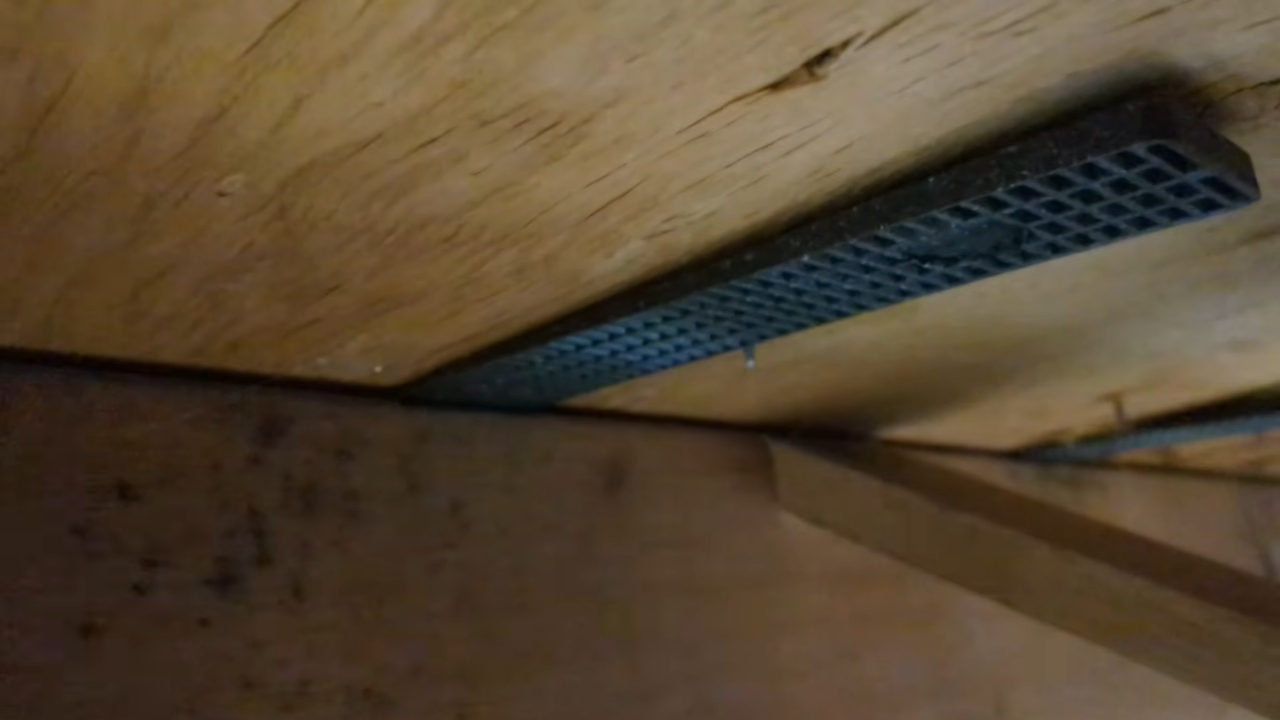 A black plastic shim installed between a wooden floor joist and the subfloor.