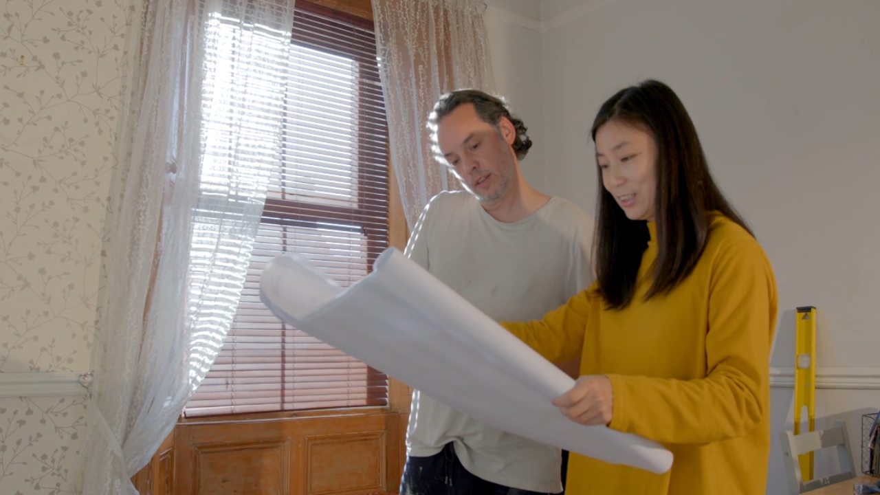 Two homeowners review renovation plans inside a room.