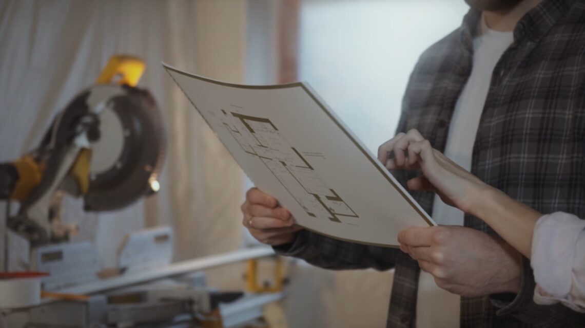 Homeowners review renovation plans beside a miter saw.