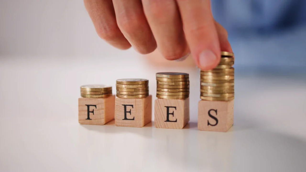 A hand adds coins to four stacks on wooden blocks that spell FEES.