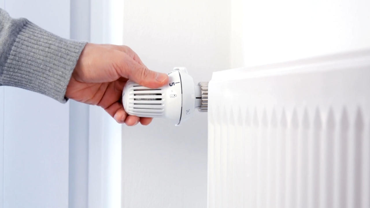 A hand adjusts the heat control on a white radiator.
